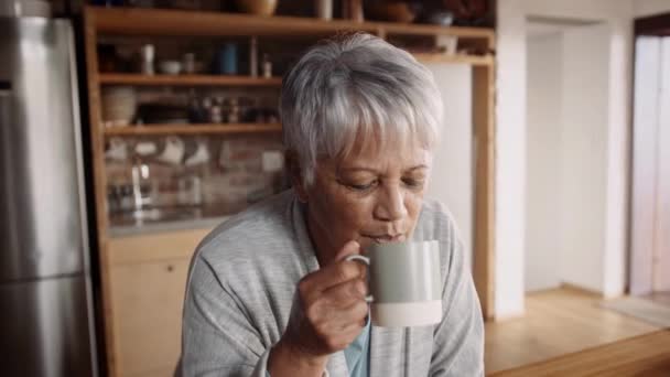 Multikulturell äldre kvinna smuttar kaffe, ler mot kameran medan i modernt kök — Stockvideo