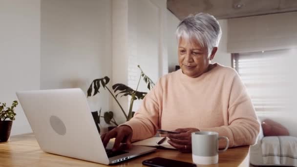 Anciana Multi-cultural mujer haciendo compra en línea utilizando el ordenador portátil y tarjeta de crédito en casa — Vídeo de stock