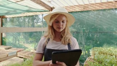 Yeşil evde çalışan beyaz kadın çiftçi dijital tablet üzerinde yazı yazıyor.