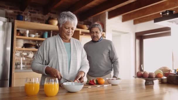 Multi-cultural elderly woman in loving relationship, chopping fruit for breakfast in modern kitchen. Joined by husband — Stock Video