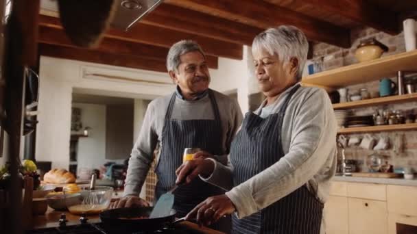 Πολυπολιτισμικό ηλικιωμένο ζευγάρι μαγειρεύει πρωινό στην κουζίνα στο φούρνο. Ευτυχείς συνταξιούχοι σύντροφοι — Αρχείο Βίντεο