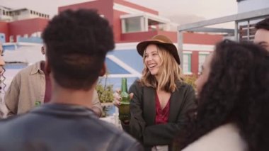 Kafkas kadın ve çok ırklı arkadaş grubu alacakaranlıktaki bir partide çatıda içkilerle sosyalleşiyorlar.