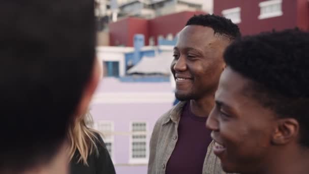 Czarny mężczyzna i wieloetniczna grupa dorosłych przyjaciół spoufalających się na dachu miasta. Uśmiech i śmiech na imprezie — Wideo stockowe