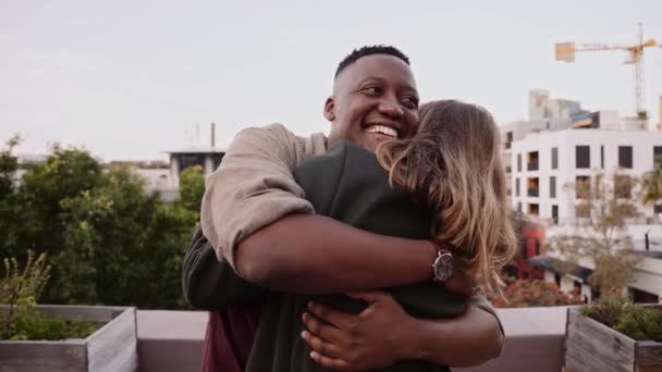 Svart man kramar och hälsar på vit kvinna på en takfest i skymningen — Stockvideo