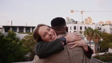 Beyaz kadın, akşam kentteki çatı partisinde siyahi erkek arkadaşını neşeyle kucaklıyor. 