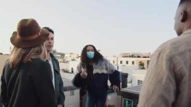 Çok kültürlü bir kadın çatıdaki partiye katılıp çeşitli yetişkin arkadaş gruplarını selamlıyor. Maskeni çıkar..
