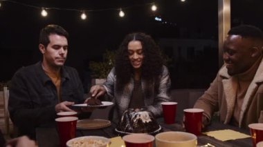 Çok kültürlü bir kadın, gece vakti çok ırklı bir grup arkadaşına doğum günü pastası ikram ediyor..