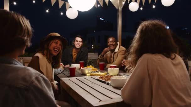 Grupo multiétnico de amigos adultos charlando en una fiesta al aire libre en una mesa en la noche — Vídeo de stock