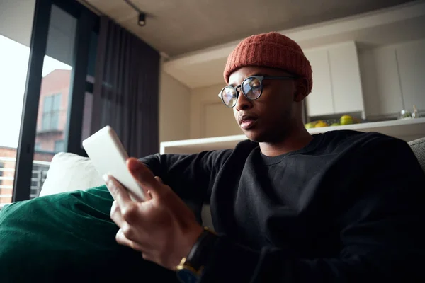 Homme noir adulte travaillant sur tablette assis dans un appartement moderne sur le canapé — Photo