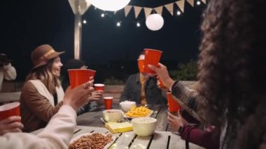 Bir grup arkadaş, akşamları çatıdaki bir partide masanın etrafında otururken birbirlerine kadeh kaldırıyorlar.