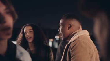 Zenci erkek, bir partinin çatısında çeşitli arkadaş gruplarıyla mutlu mesut sosyalleşiyor.