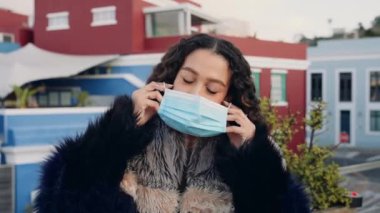 Karışık ırktan yetişkin bir kadın alacakaranlıkta şehrin çatısında maske takıyor. Arkaplanda renkli şehir manzarası