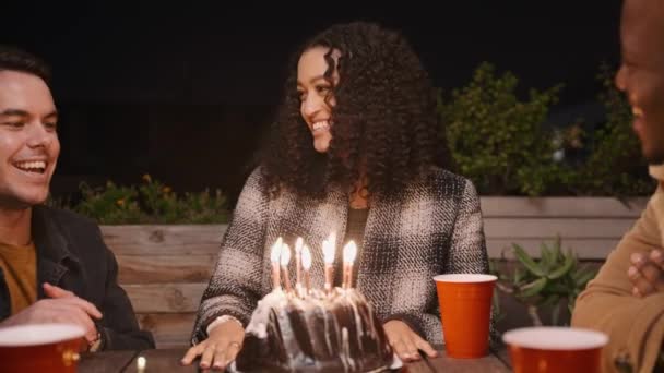 Mujer multicultural sonriendo y soplando velas en su pastel de cumpleaños mientras grupo multiétnico de amigos cantan feliz cumpleaños — Vídeos de Stock