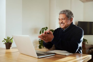 Mutlu çok kültürlü yaşlı erkekler online olarak ailesiyle görüşüyor. Modern evde izole edilmiş, mutfak tezgahında oturuyor..