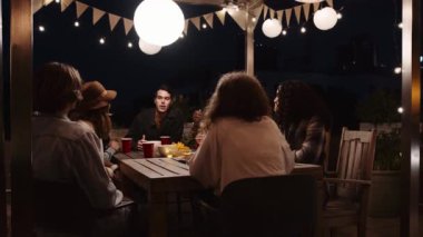 Kafkas erkek ve çeşitli yetişkin arkadaş grupları gece vakti açık bir masada bir partide sohbet ediyorlar.