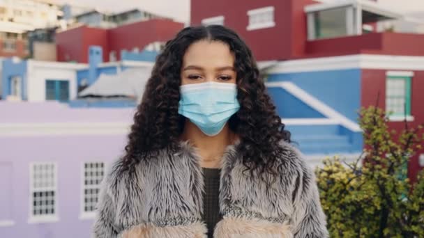 Karışık ırktan yetişkin bir kadın alacakaranlıkta şehrin çatısında maskesini çıkarıyor. Arkaplanda renkli şehir manzarası — Stok video