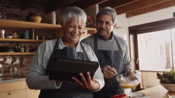 Multi-kulturní starší pár vaření vajec a s odkazem na recept na elektronické tablety v moderní kuchyni — Stock video