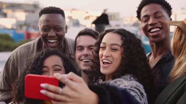 Diverso grupo de amigos adultos tomando un selfies en un teléfono celular, riendo en una azotea en una fiesta al atardecer — Vídeos de Stock