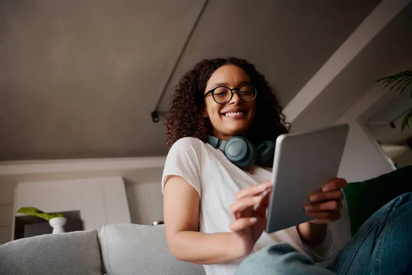 Multikulturelle junge erwachsene Frau lacht mit Tablet auf modernem Sofa — Stockfoto