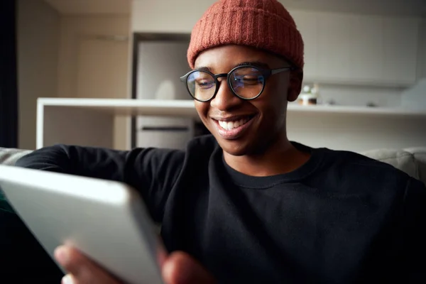 Close up de adulto macho preto sorrindo enquanto olha para tablet. Apartamento moderno no sofá — Fotografia de Stock