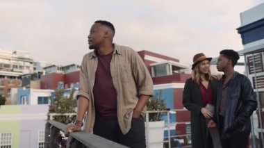 Zenci erkek, şehrin çatı katındaki balkondan çok ırklı bir arkadaş grubuyla manzaraya hayran..