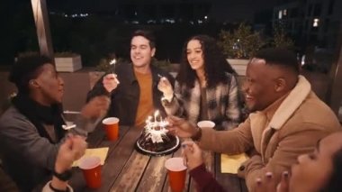 Çeşitli arkadaşlar ellerinde maytaplarla doğum günü şarkısı söylüyorlar. Geceleri çatıdaki bir masanın etrafında oturmak..