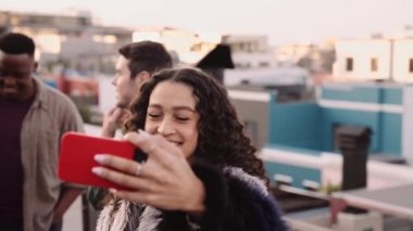 Karışık ırktan yetişkin bir kadın gülümsüyor. Akşam karanlığında şehirdeki bir partide çatıda selfie çekiyor.