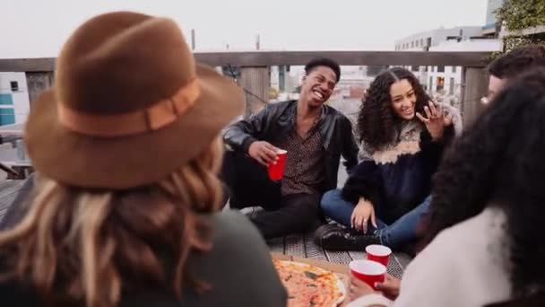 Group of young multi-ethnic friends laughing at jokes at a party on a rooftop at dusk — Stockvideo