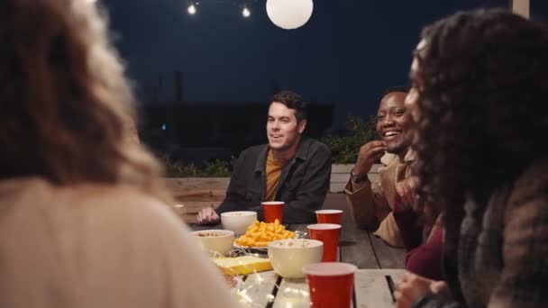 Diverso grupo de amigos adultos socializando alrededor de una mesa en una fiesta en la azotea de la ciudad — Vídeo de stock