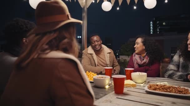 Мультиэтническая группа взрослых друзей, общающихся за столом на вечеринке на крыше в городе — стоковое видео