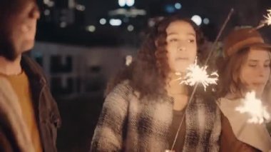 Çok kültürlü bir kadın ve beyaz bir kadın dans ediyor ve çeşitli arkadaşlarıyla iyi vakit geçiriyor. Gecenin bir yarısında çatıda ellerinde maytaplar var..