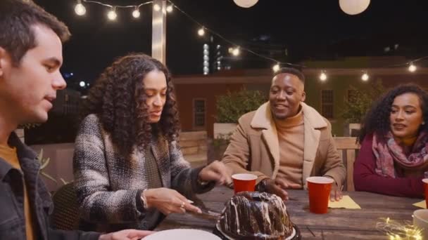 Hembra multicultural sirviendo pastel de cumpleaños a su grupo multiétnico de amigos. Sentado en una mesa en una fiesta en la azotea. — Vídeo de stock