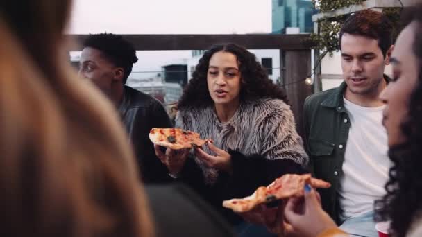 Multikulturell kvinnlig och mångsidig grupp vuxna vänner chattar, äter pizza på ett tak i skymningen. Högkvalitativ 4K-film — Stockvideo