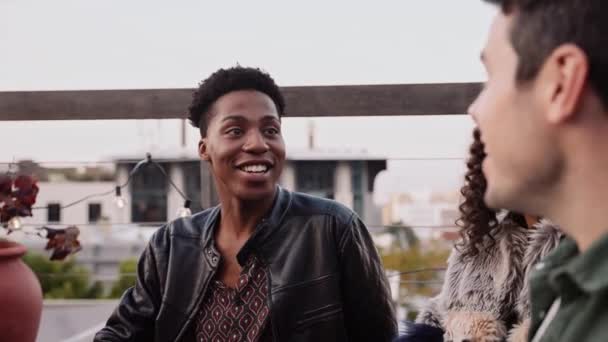 Young black adult man in conversation with diverse group of friends at a rooftop party — Video Stock