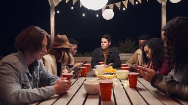 Καυκάσιος άντρας κάθεται μόνος του, ενώ η πολυεθνική ομάδα φίλων του στέλνει μήνυμα σε πάρτι στην ταράτσα. — Αρχείο Βίντεο