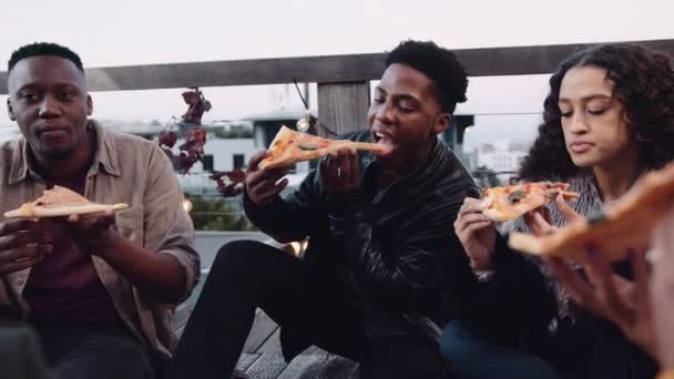 Diverso grupo de amigos adultos charlando, comiendo rebanadas de pizza en una azotea a la luz de la noche. Imágenes 4K de alta calidad — Vídeos de Stock