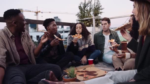 Różnorodna grupa dorosłych przyjaciół rozmawiających, jedzących pizzę na dachu w wieczornym świetle. Wysokiej jakości materiał 4K — Wideo stockowe