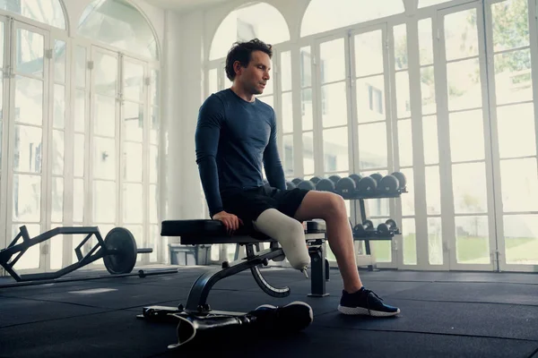 Mann mit Beinprothese auf einer Gymnastikbank. Er bereitet sich mental auf seine Fitnesseinheit vor — Stockfoto