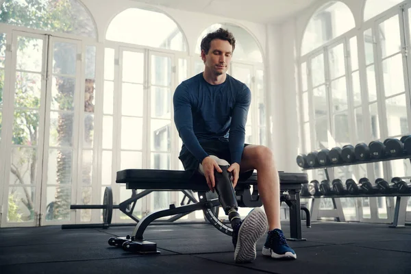 Disabled male athlete putting on his prosthetic leg in the gym — Stock Photo, Image