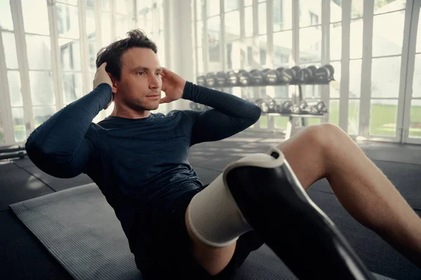 Man with prosthetic leg performing crunches in a gym . Paralympic athlete — Stock Photo, Image