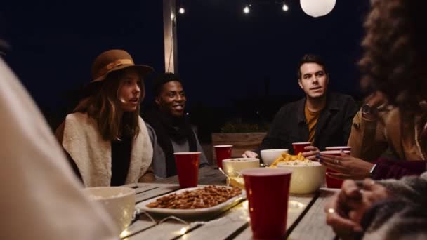 在户外的一个宴会上，一群不同的朋友在餐桌边聊天、大笑、吃零食 — 图库视频影像