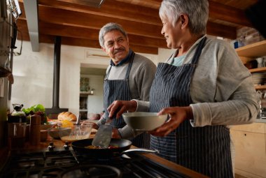 Modern mutfakta sağlıklı kahvaltı hazırlarken birbirine gülümseyen çok ırklı yaşlı bir çift..