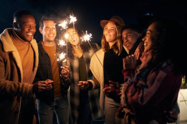 Çok kültürlü genç yetişkinlerden oluşan farklı bir grup bir partide birlikte maytap yakıyorlar. İyi zamanlardı, arkadaşlarla birlikte..