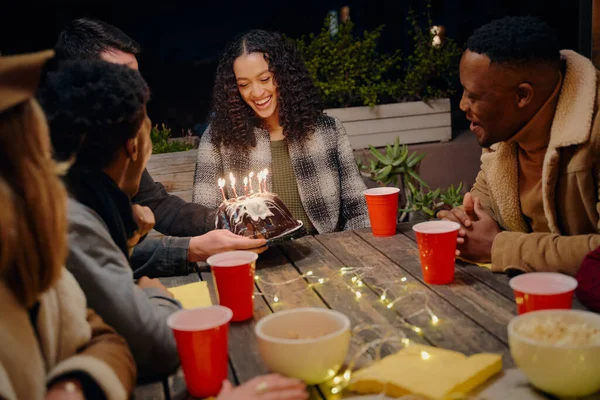 Cumpleaños niña sonriendo como grupo de diversos adultos jóvenes celebran su cumpleaños en la fiesta en la azotea con pastel —  Fotos de Stock