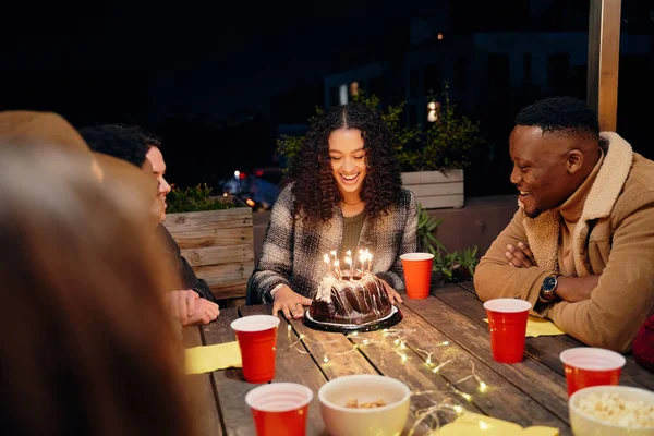 Grupa różnorodnych młodych osób świętujących birasowe urodziny kobiet, siedzi na modnej imprezie na dachu świętując urodziny dziewczyny z tortem. — Zdjęcie stockowe