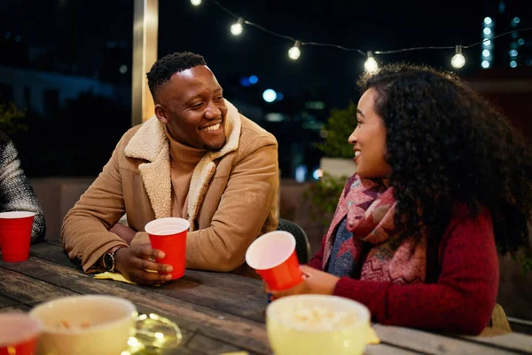Mujer birracial y hombre negro hablando en una fiesta en la azotea de la ciudad. De moda, beber con tazas rojas. —  Fotos de Stock