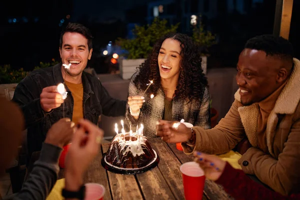 Grupo de diversos adultos jóvenes sentados en la azotea temática boho fiesta de cumpleaños iluminación chispas de pastel. — Foto de Stock