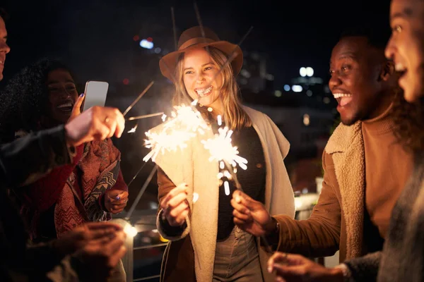 在城市的夜生活中，一群年轻的成人多元文化的朋友在一个屋顶的派对上点燃着火花。为社交媒体拍照 — 图库照片