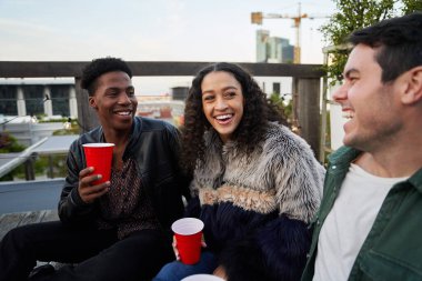 Bir grup çok kültürlü yetişkin şehrin çatı katındaki bir partide otururken birlikte şakaya gülüyorlar..