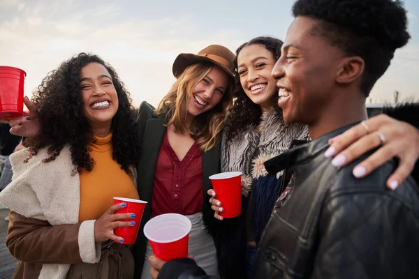 Portrait d'un groupe diversifié d'amis embrassant tout en souriant à la caméra. Rire et socialiser sur le toit-terrasse le soir — Photo